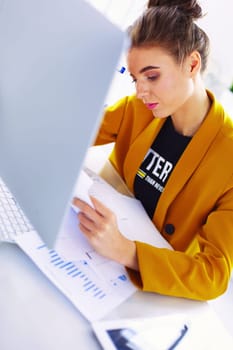 Beautiful young businesswoman doing some paperwork while sitting at office desk in front of laptop