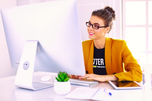 Young confident businesswoman working at office desk and typing with a laptop.