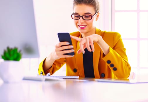 Portrait of businesswoman using mobile phone and text messaging while sitting at desk in front of laptop