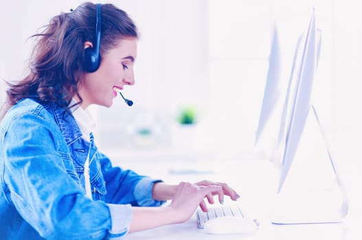 Happy charming young woman sitting and working with laptop using headset in office.