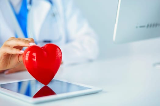 Female doctor with stethoscope holding heart, on light background.