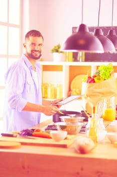 Man following recipe on digital tablet and cooking tasty and healthy food in kitchen at home.