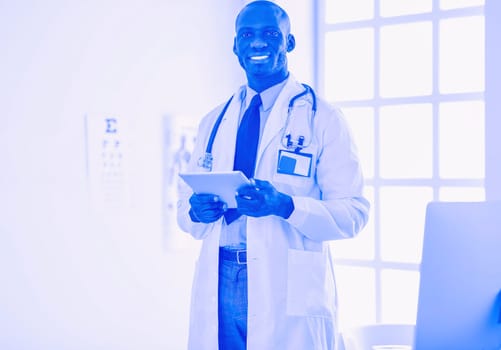 Male black doctor worker with tablet computer standing in hospital.