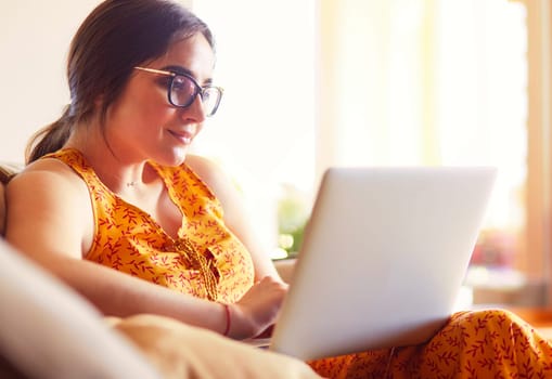 Young woman sitting on couch working on laptop computer at home.