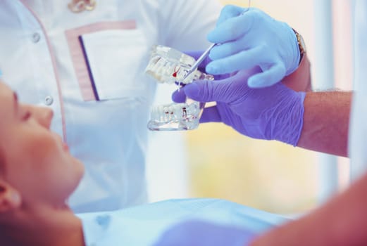 Senior male dentist in dental office talking with female patient and preparing for treatment.