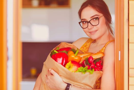 Young woman holding grocery shopping bag with vegetables.