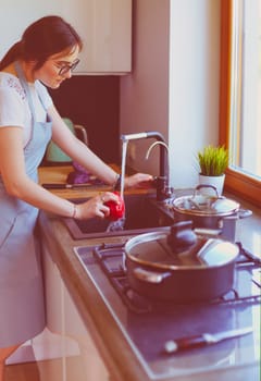 Woman washing vegetables. Beautiful young woman washing vegetables for salad and smiling while standing in the kitchen.