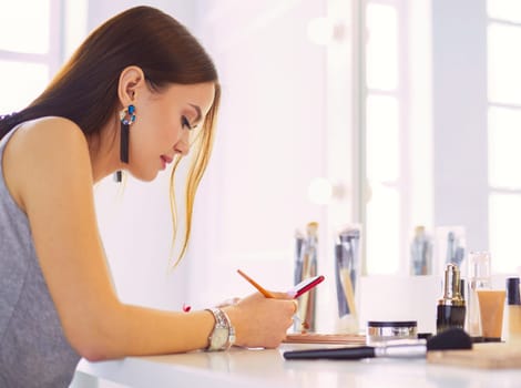 A beautiful young woman sitting at a makeup table and doing her makeup
