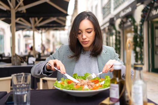 Portrait attractive woman in glasses eating salad at cafe table. Beautiful young female enjoying fresh salad at nice restaurant.