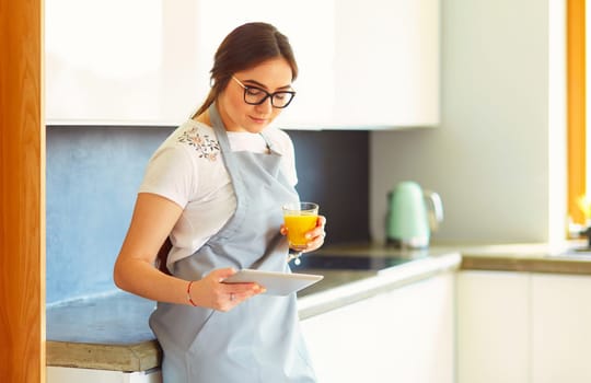 Young woman with orange juice and tablet in kitchen.