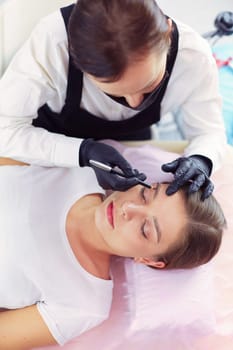 Cosmetologist applying permanent make up on eyebrows.