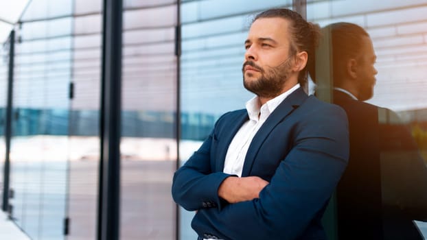 Confidence successful businessman in suit with beard standing in front of office glass building lean on wall arm crossed. Hispanic handsome business man looking away. Portrait shoot. Banner