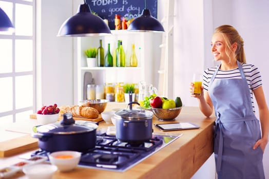 Attractive woman holding a glass of orange juice while standing in the kitchen.