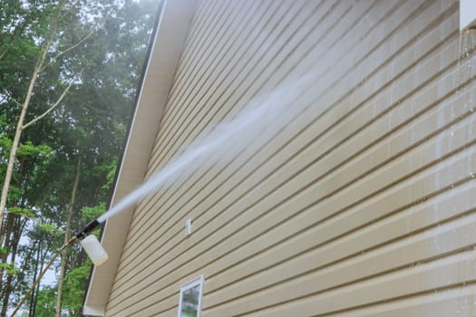 Service man in washing siding houses by using high pressure nozzles spray water soap cleaner