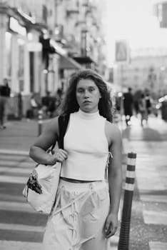 A stylish girl in white clothing with curly hair on the city streets. High quality photo