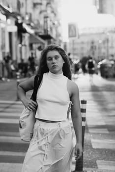 A trendy girl in a white outfit and curly hair on the city streets. High quality photo