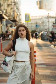 A chic girl wearing white clothes and sporting curly hair on the city streets. High quality photo