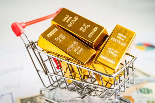 Gold bar in shopping cart on US dollar banknotes money and graph, economy finance exchange trade investment concept.