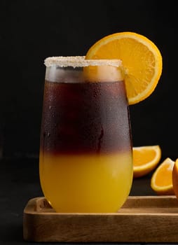 Iced coffee with orange juice in a transparent glass, refreshing bumble coffee on the table, black background