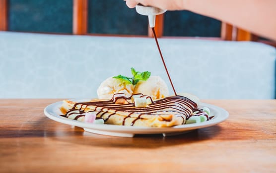 Chocolate crepe with ice cream on wooden background. Close up of sweet crepe with ice cream