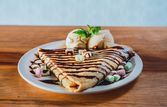 Close up of sweet crepe with ice cream on wooden table. Chocolate crepe with ice cream on wooden background