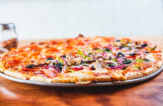 Delicious Supreme Pizza and pepperoni on wood with copy space. Close up of supreme pizza with olives on wooden table