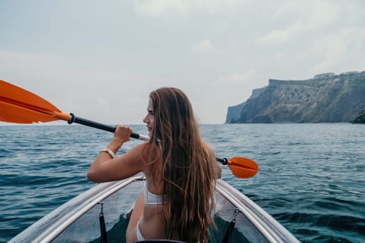 Woman in kayak back view. Happy young woman with long hair floating in transparent kayak on the crystal clear sea. Summer holiday vacation and cheerful female people having fun on the boat.