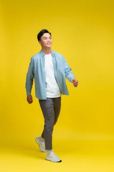 young asian man go walk step look empty space isolated over yellow background