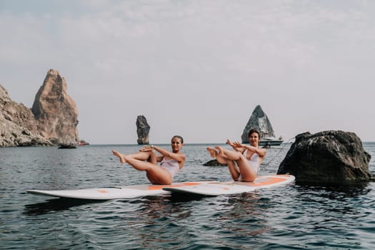 Woman sup yoga. Middle age sporty woman practising yoga pilates on paddle sup surfboard. Female stretching doing workout on sea water. Modern individual hipster outdoor summer sport activity