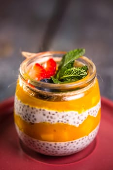 close-up of a healthy dessert in a glass jar with mango, chia seeds and delicate cream.