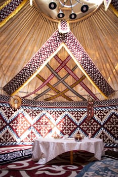 the interior of the national traditional Kazakh festive yurt with patterns and a table.