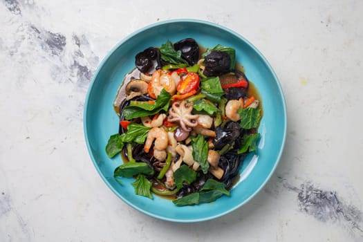 salad with seafood and black mushroom in a blue plate top view.