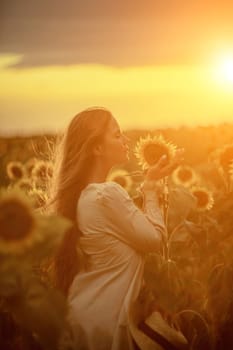 Beautiful middle aged woman looks good in a hat enjoying nature in a field of sunflowers at sunset. Summer. Attractive brunette with long healthy hair