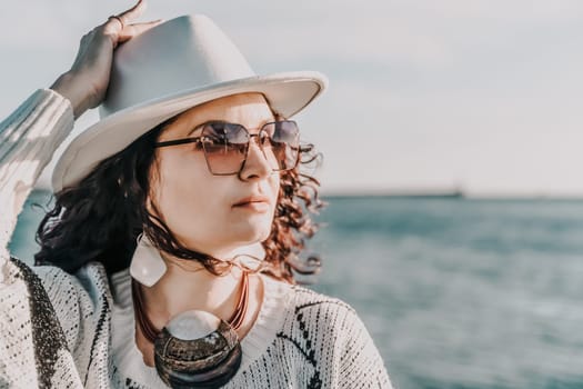 Portrait of a curly haired woman in a white hat and glasses on the background of the sea