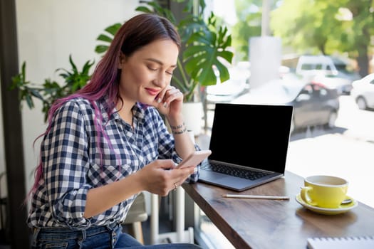 Rear shot of female student learning online via laptop before her lectures. Woman typing on notebook with blank screen with copy space for your text or advertising content, sitting at wooden table