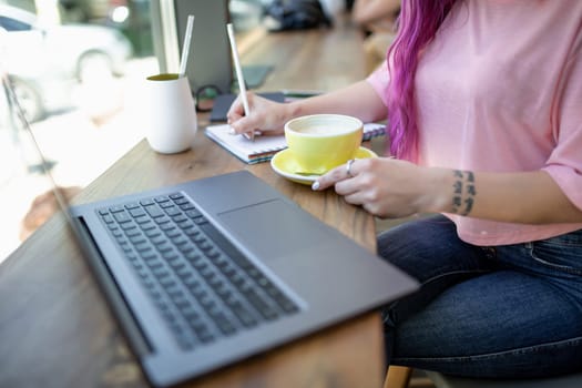 Rear shot of female student learning online via laptop before her lectures. Woman typing on notebook with blank screen, sitting at wooden table