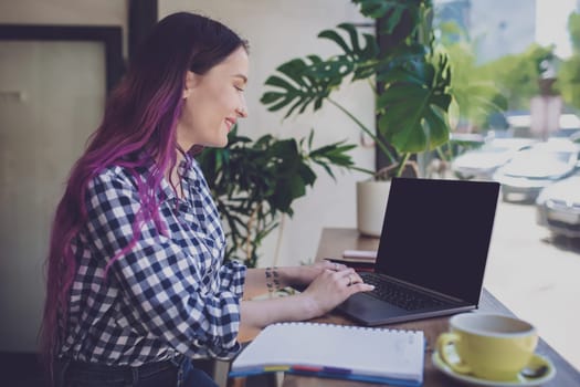Rear shot of female student learning online via laptop before her lectures. Woman typing on notebook with blank screen with copy space for your text or advertising content, sitting at wooden table