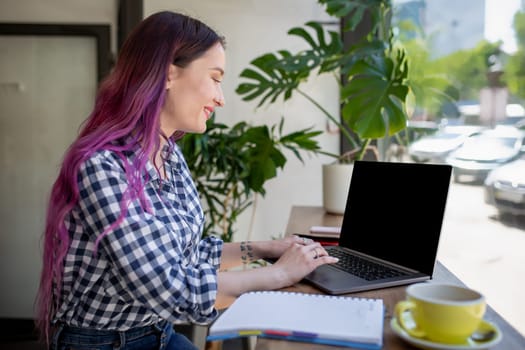 Rear shot of female student learning online via laptop before her lectures. Woman typing on notebook with blank screen with copy space for your text or advertising content, sitting at wooden table