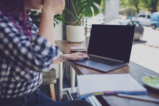 Rear shot of female student learning online via laptop before her lectures. Woman typing on notebook with blank screen with copy space for your text or advertising content, sitting at wooden table