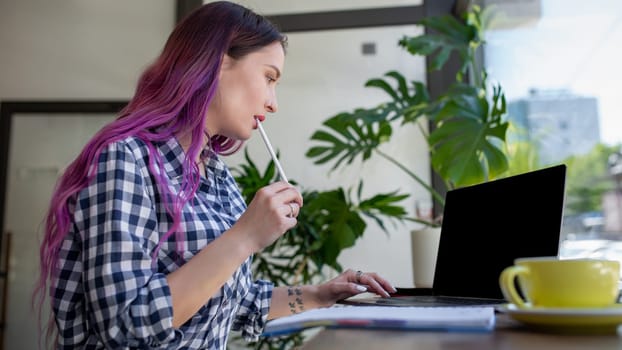 Rear shot of female student learning online via laptop before her lectures. Woman typing on notebook with blank screen with copy space for your text or advertising content, sitting at wooden table