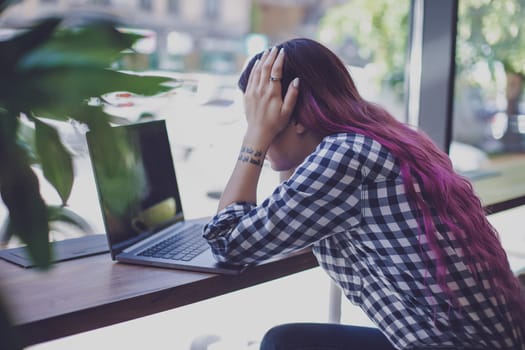 Rear shot of female student learning online via laptop before her lectures. Woman typing on notebook with blank screen, sitting at wooden table