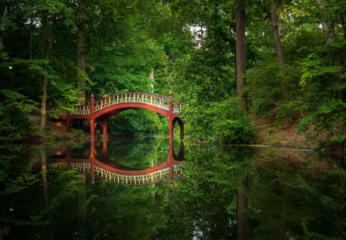 Ornate wooden bridge over very calm Crim Dell pond on campus of William and Mary college in Williamsburg Virginia