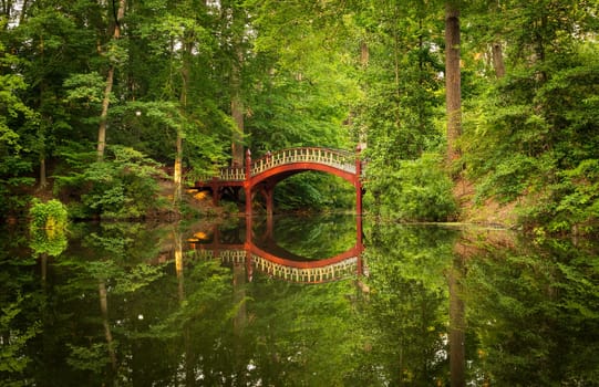 Ornate wooden bridge over very calm Crim Dell pond on campus of William and Mary college in Williamsburg Virginia