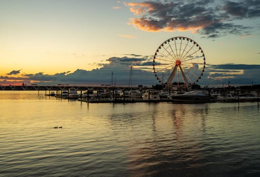 Illuminated ferris wheel at National Harbor near the nation capital of Washington DC at sunset with marina in the foreground