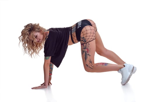Young beautiful caucasian blonde girl with tattoo on her legs, wearing black booty shorts and fishnet dancing twerk isolated on white background