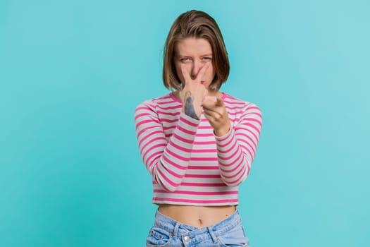 I am watching you. Young confident woman pointing at her eyes and camera, show I am watching you gesture, spying on someone. Pretty attractive girl in crop top isolated alone on blue studio background