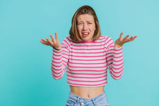 What Why. Sincere irritated young woman raising hands in indignant expression, ask reason of failure demonstrating disbelief irritation by trouble. Pretty confused girl in crop top on blue background