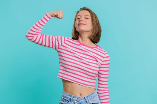 I am strong and independent. Young woman showing biceps and looking confident, feeling power strength to fight for rights, energy to gain success win. Girl isolated alone on blue studio background