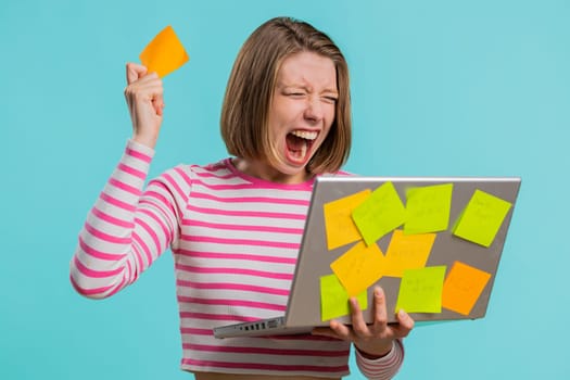 Exhausted freelancer woman with pasted sticker notes use laptop computer having concentration problem creative crisis, time out. Nervous girl confused by big routine work loading on blue background
