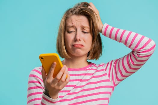 Woman use mobile phone smartphone typing browsing, loses becoming surprised sudden lottery results, bad fortune, loss, fail. Pretty girl in crop top isolated alone on blue studio background, indoors